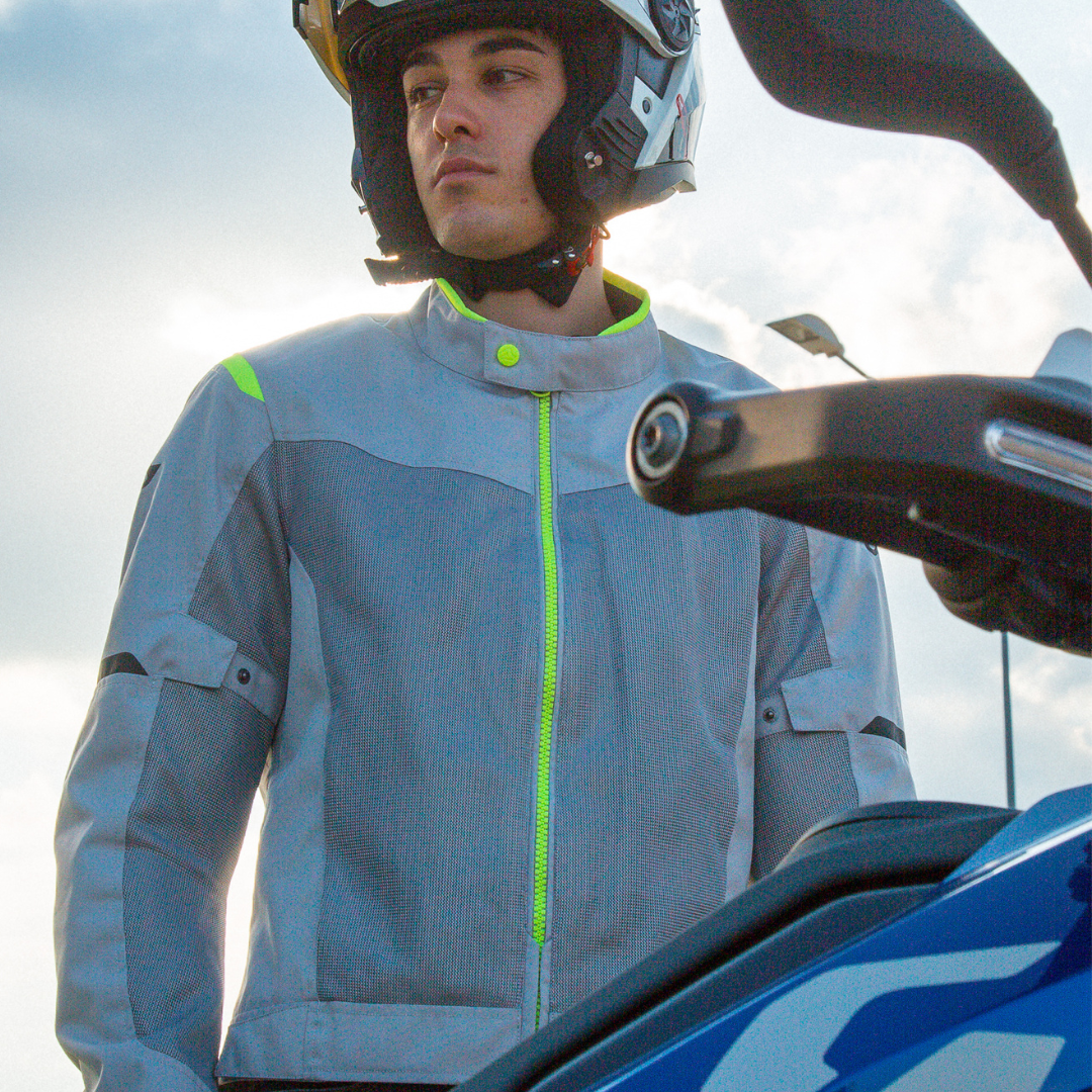 Person wearing a motorcycle helmet and jacket next to a motorcycle with a cloudy sky background