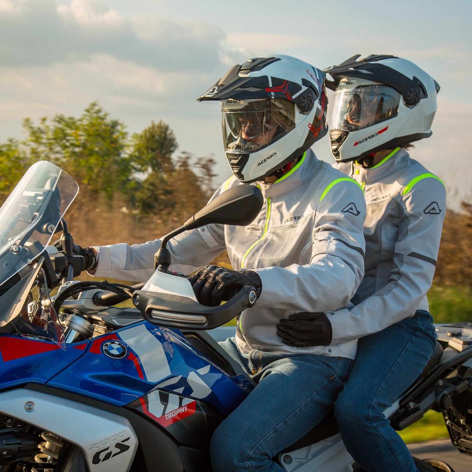 Two people riding a motorcycle on a road with trees in the background