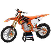 A detailed model or toy motocross dirt bike in orange, white, and black, displayed on a black stand against a light gray background.
