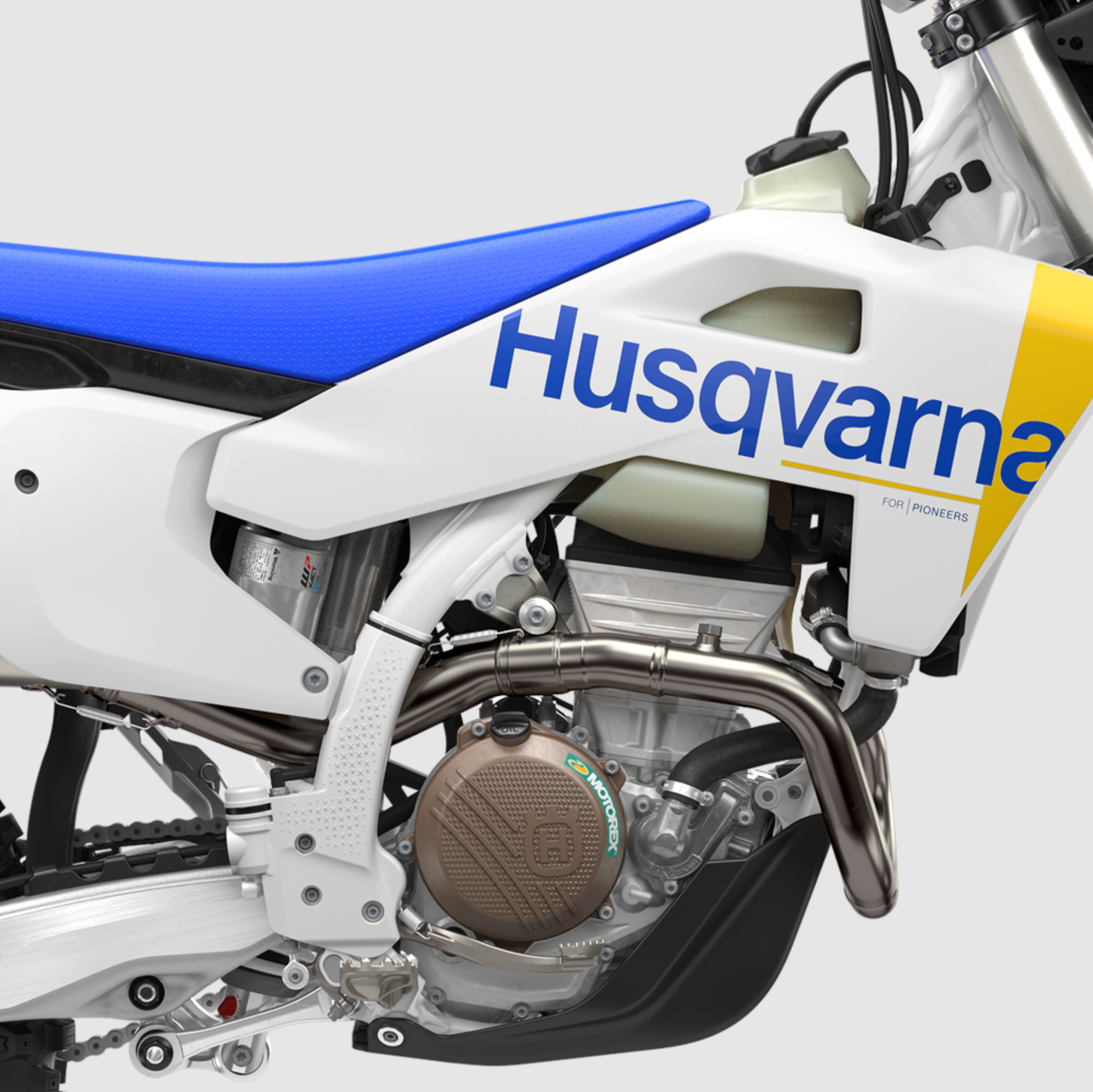 Close-up of a white and blue Husqvarna dirt bike or motorcycle bodywork, showing the side panel with the Husqvarna logo, blue seat, yellow graphic, and exposed engine components against a light gray background.