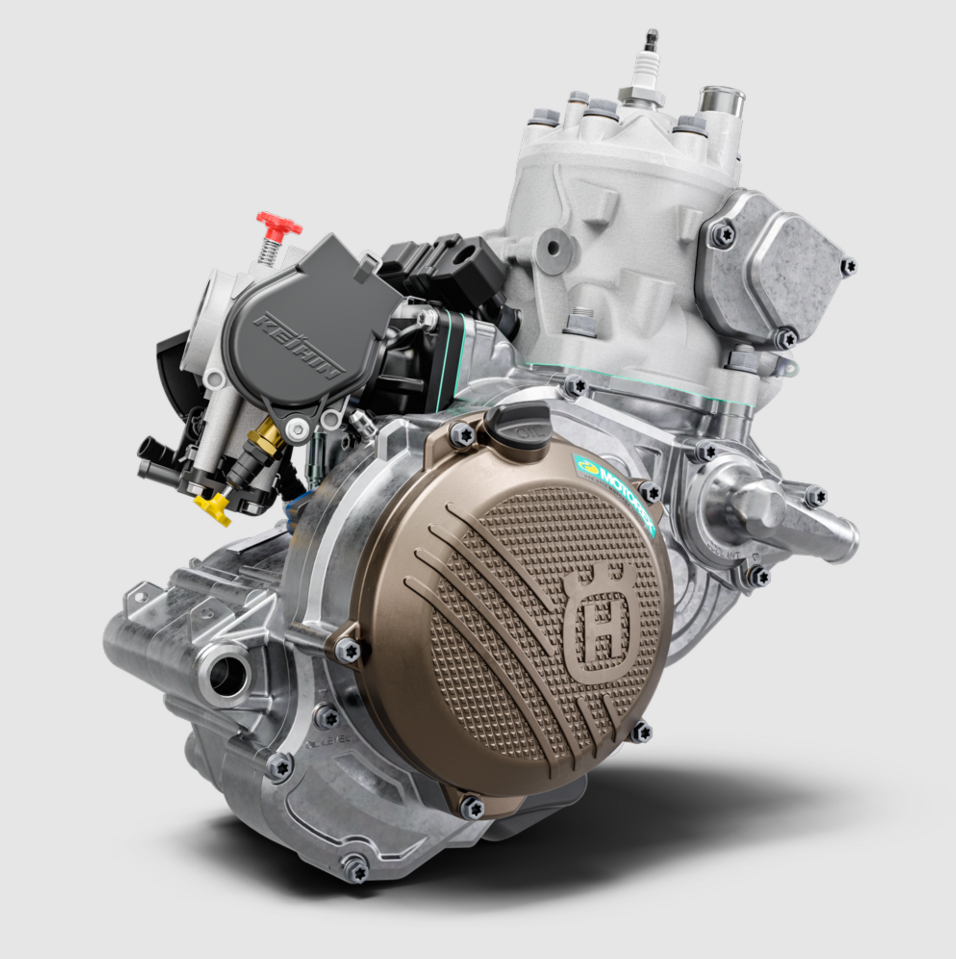 A high-performance motorcycle engine with a prominent bronze-colored crankcase cover, silver aluminum components, and a black fuel injection cover, shown on a light gray background.