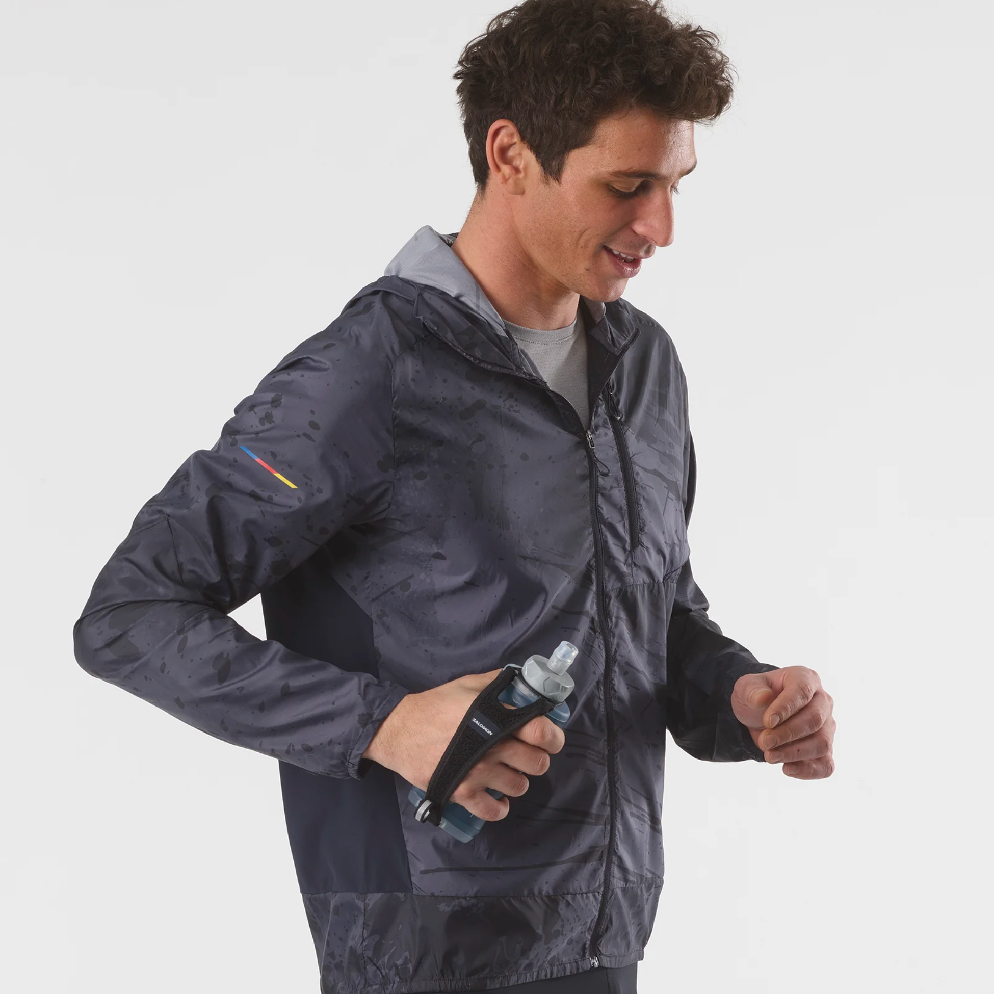 Man wearing a dark gray jacket holding a water bottle on a white background