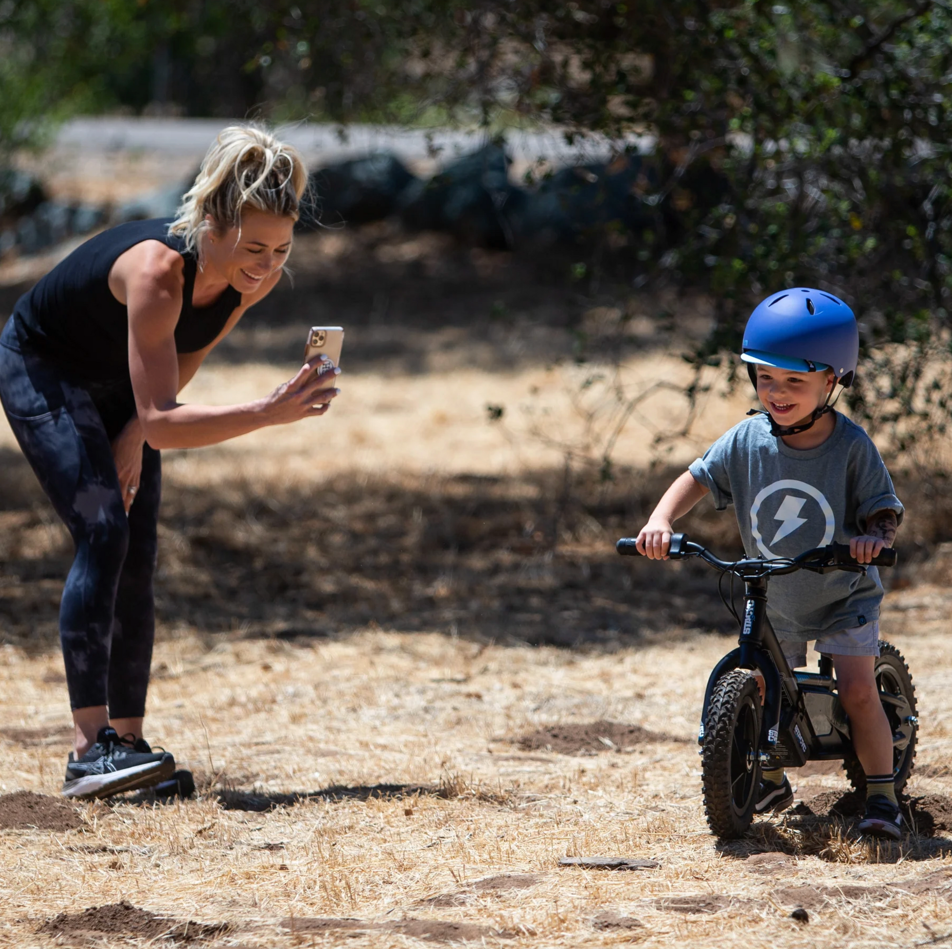 Woman taking a photo of a child on a bike in an outdoor setting